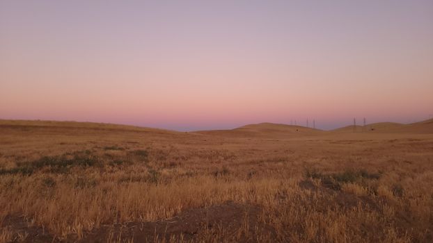 A peaceful sunset over rolling brown fields under a pastel sky, ideal for natural themes.