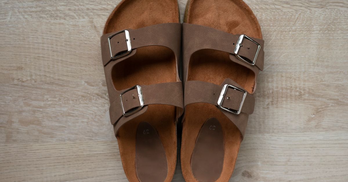 Close-up of stylish brown leather sandals with silver buckles on wooden floor.