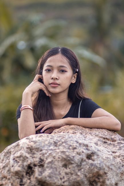 Young woman leaning on rock with hand on cheek, outdoors.