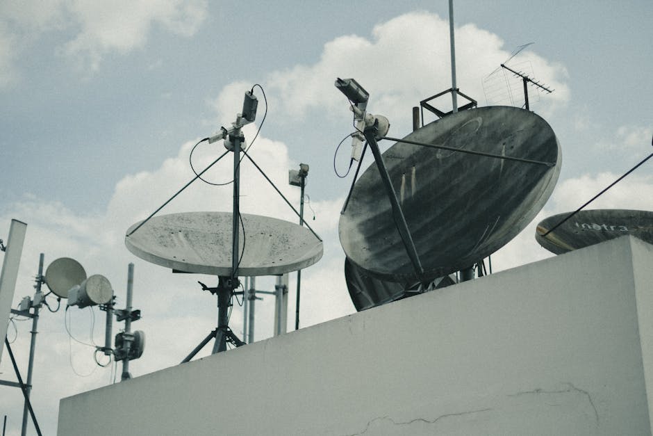 A detailed view of satellite dishes and antennas on an urban rooftop under a cloudy sky.