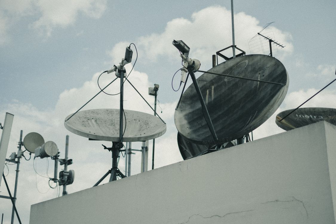 Satelitske antene i komunikacijska oprema na gradskom krovištu pod oblačnim nebom