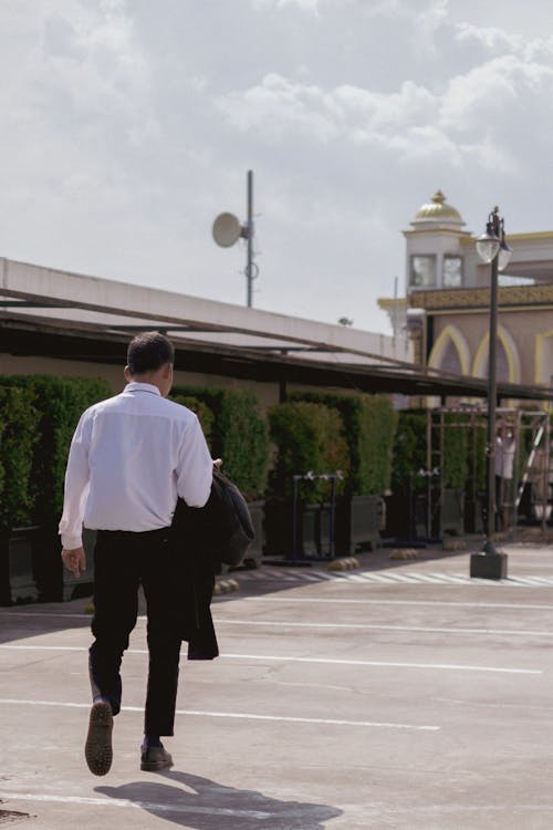 A Person in White Dress Shirt and Black Pants Walking Near Building