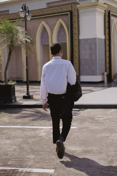Back View of a Man in White Long Sleeves Walking on the Street