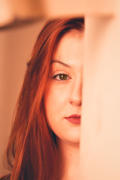 Free Artistic close-up of a red-haired woman half-hidden behind a wall, highlighting beauty and mystery. Stock Photo