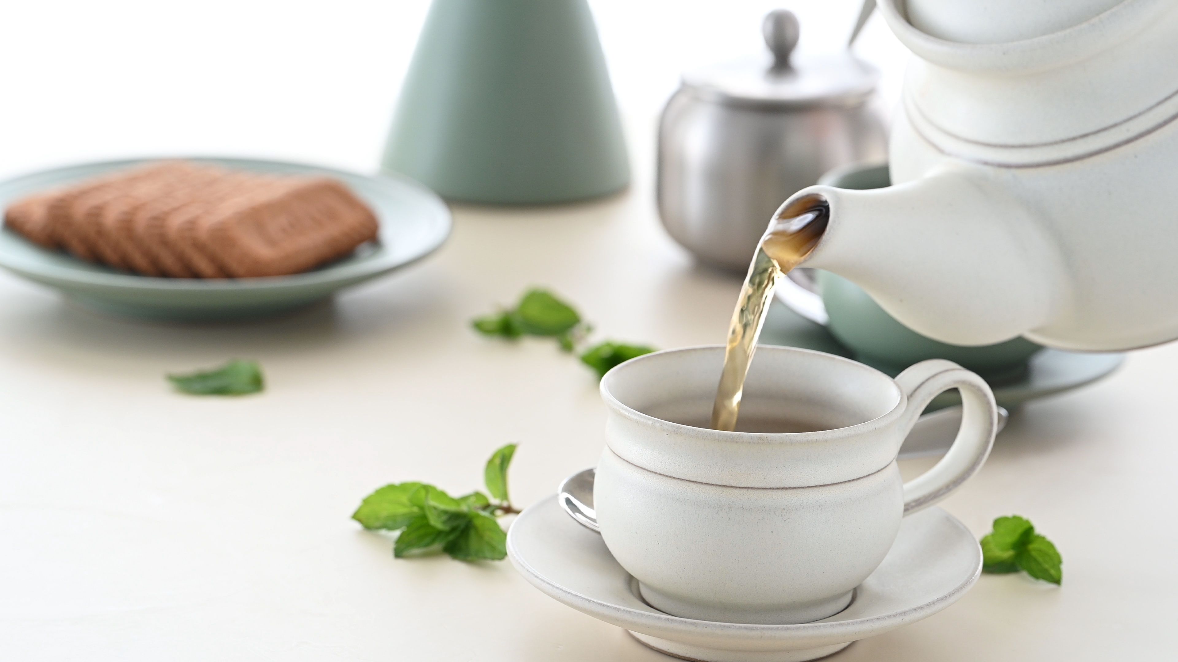 A refined tea setup with warm tea being poured, accompanied by biscuits and mint leaves.
