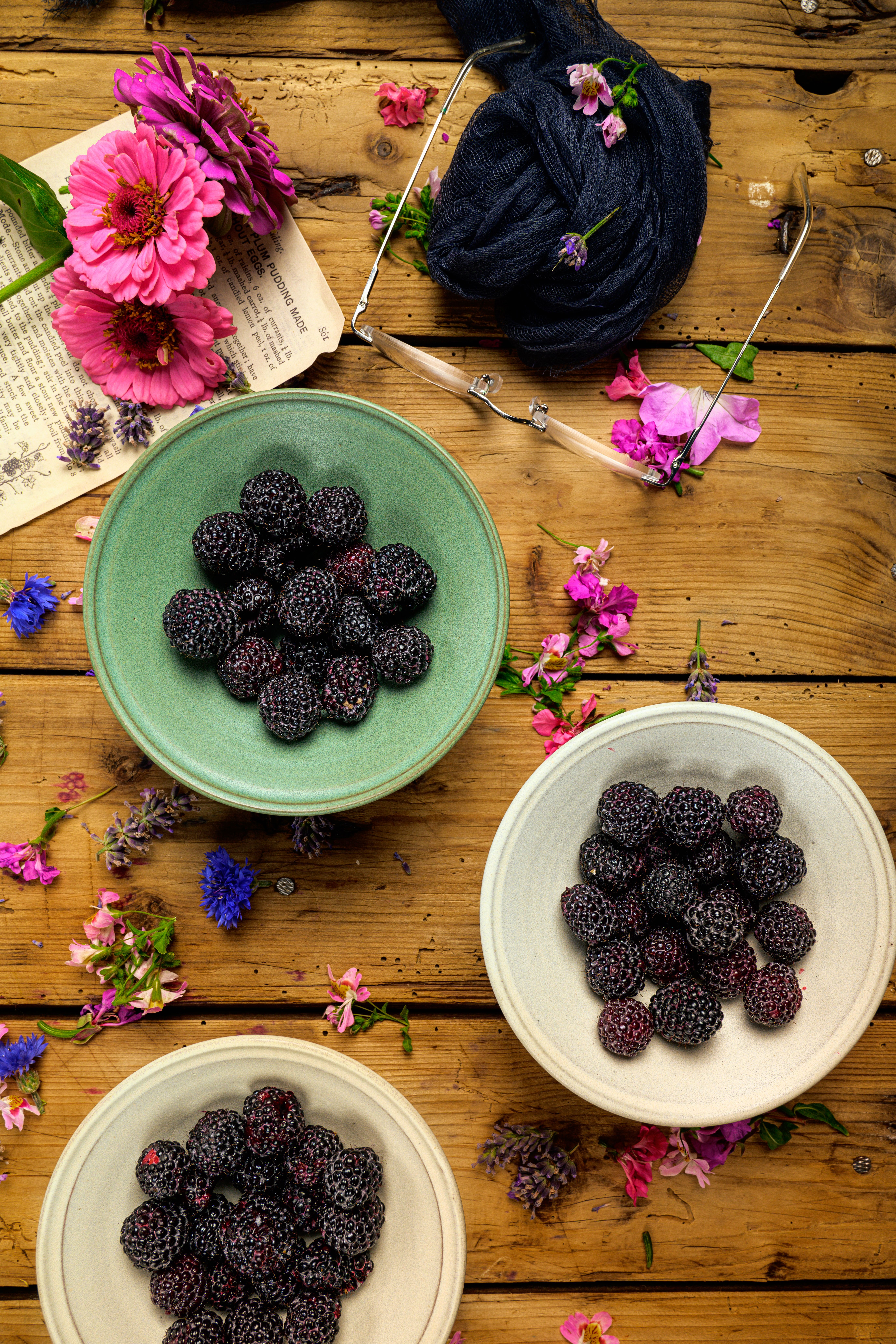 A vibrant display of blackberries in ceramic bowls adorned with pink flowers on a wooden surface.