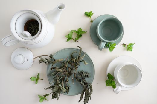 Aesthetic top view of a teapot with cups and dried herbal tea leaves on a light background.