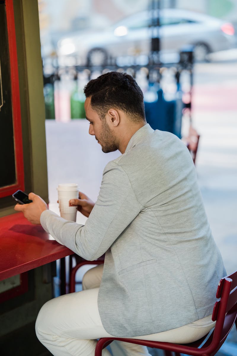 Professional using a smartphone at an outdoor cafe table with coffee, browsing apps