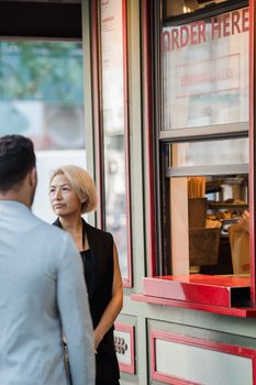 Two people wait to order at an outdoor bakery window, enjoying the urban setting.
