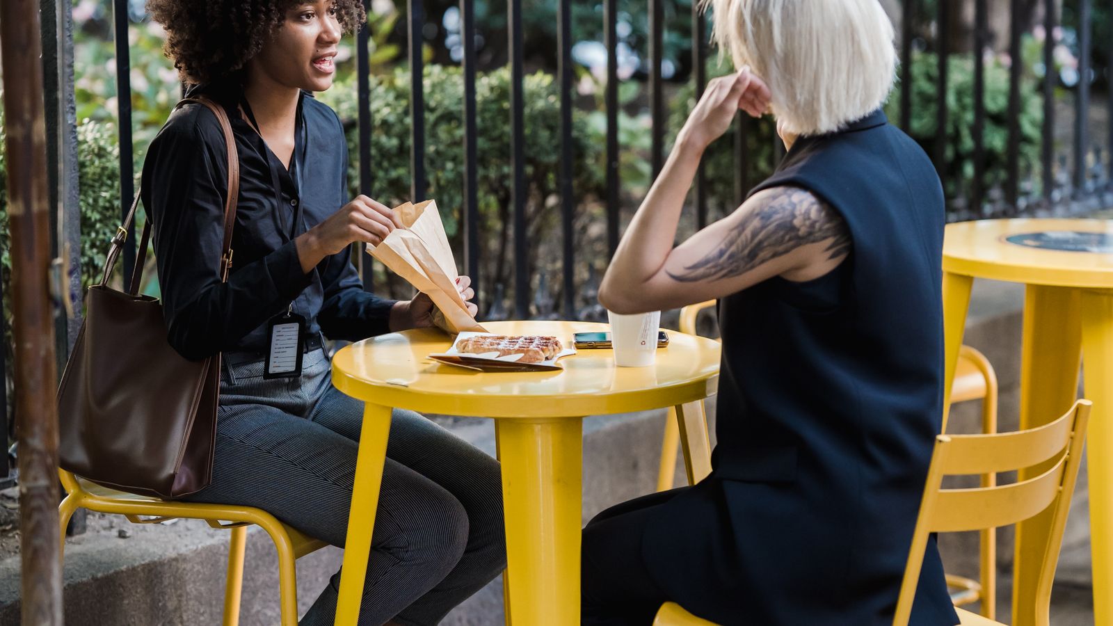 Two people talking at an outdoor café with yellow chairs