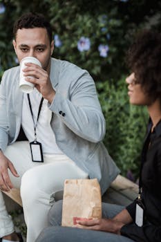 Two professionals in a garden setting taking a coffee break with disposable cups and ID badges.
