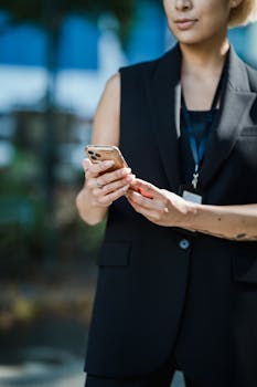 Midsection view of a woman using a smartphone outdoors with a blurred city background.