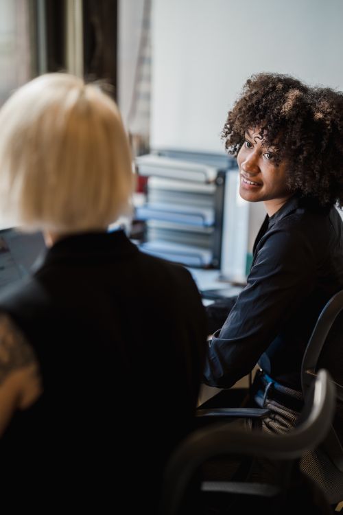 Free Two professional women engaging in conversation at an office desk, fostering teamwork. Stock Photo