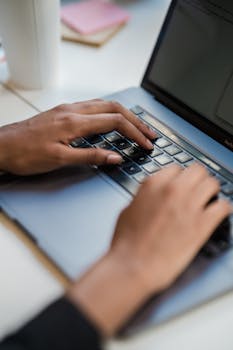A closeup image showing hands typing on a laptop keyboard in an office setting.