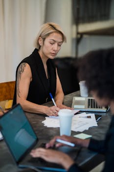 Diverse team collaborating around a table in an office setting with technology and paper documents.