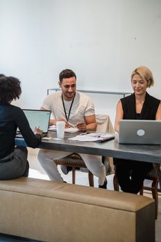 Three colleagues in a modern office space having a team meeting with laptops.