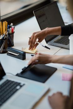 Close-up of hands using office supplies on a desk with laptops and stationery.