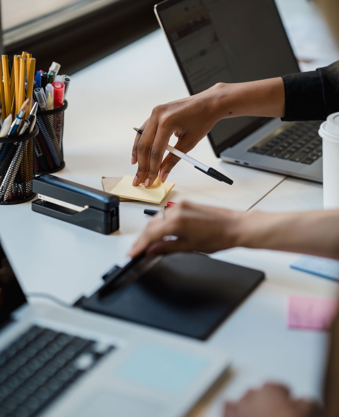 Hands working together across laptops and notes at a bright desk