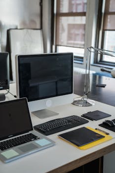 A well-organized office desk with a desktop, laptop, and office supplies in a bright workspace.