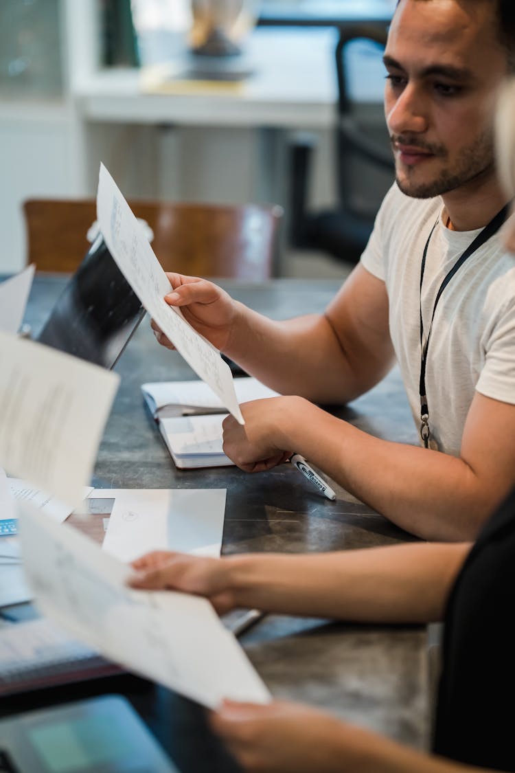 Close Up Of People At Office Desk Looking Together At Papers