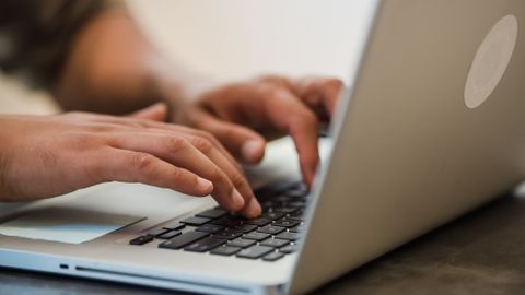 Adult typing on a laptop keyboard indoors, focused on work and technology.
