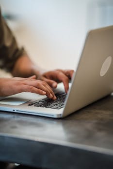 Adult typing on a laptop keyboard indoors, focused on work and technology.