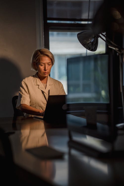 Vertical Shot of a Woman Using Laptop in a Dark Office