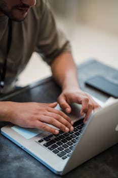 Close up of hands typing on a laptop keyboard in an indoor office environment.