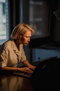 A businesswoman deeply engaged in work while typing on a laptop in a dimly lit office environment.