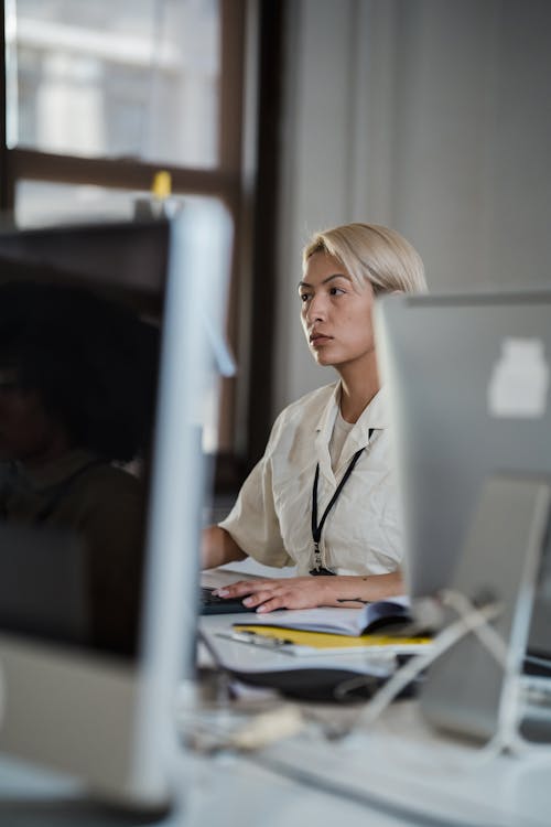 Vertical Shot of a Blond Woman between Computer Screens in an Office