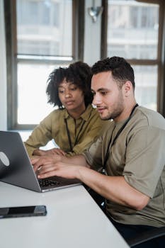 Two colleagues working collaboratively on a laptop in an office.