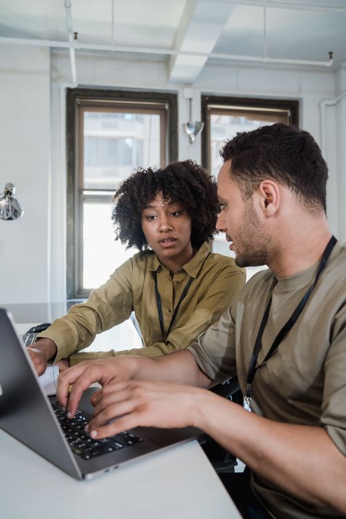 Two colleagues working together on a laptop in a small, bright office