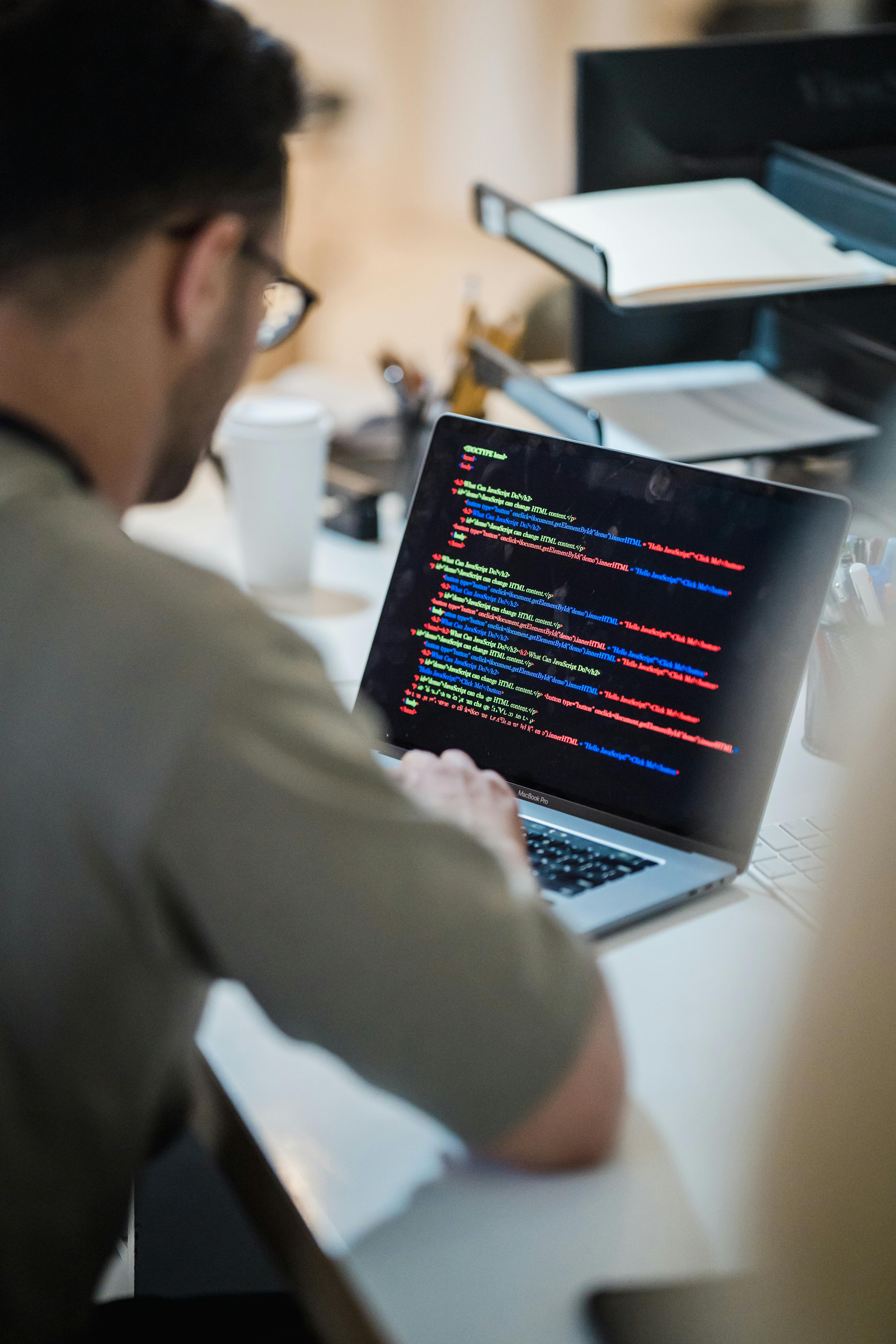 vertical shot of a man in a beige t shirt looking at laptop screen with multicoloured code