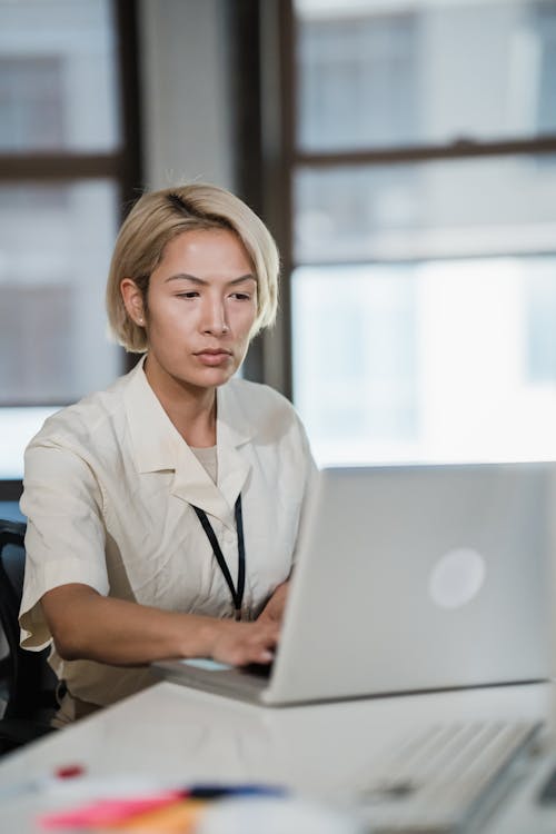 Vertical Shot of a Blonde Woman Working in an Office Using a Laptop