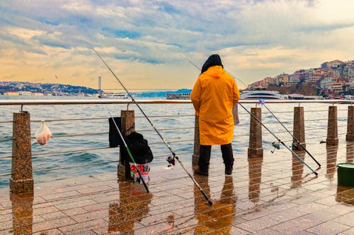 A Person in  Orange Raincoat Standing on Concrete Dock