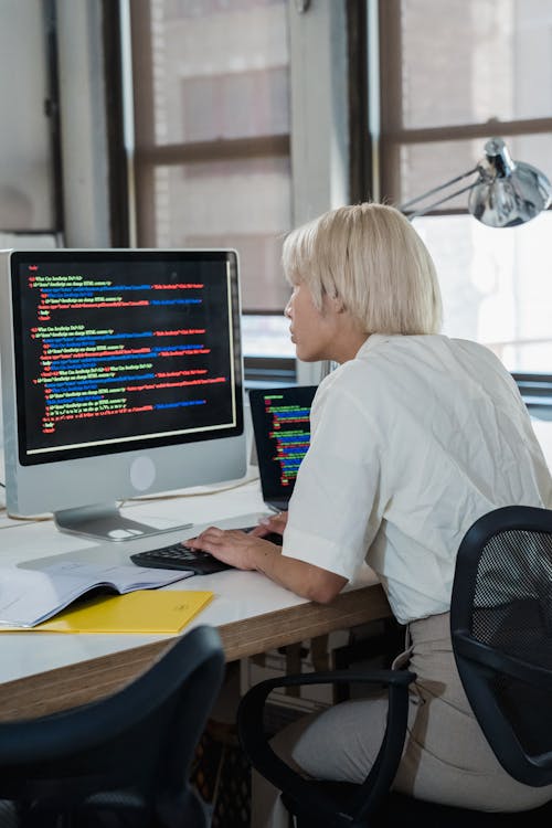 Blonde Woman Reading Multicoloured Code on a Computer Screen