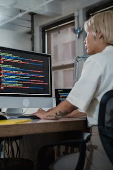 Woman programming at desk with multiple monitors in a modern office setting.