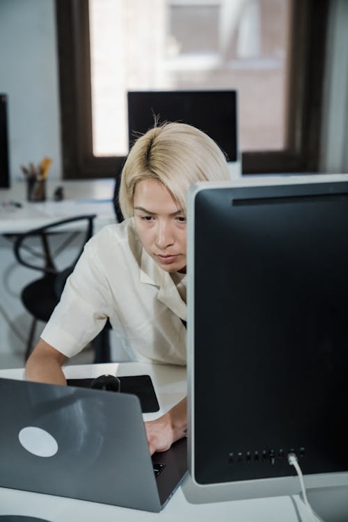 Vertical Shot of a Blond Woman Using Two Computer Screens