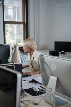 Blonde woman working at computer in a modern office setting.