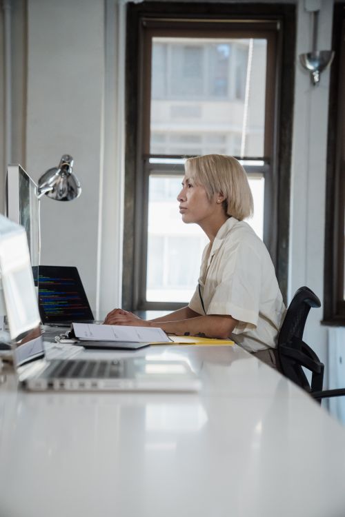 Free A woman with blonde hair works intently at a desk in an office setting, using a laptop. Stock Photo