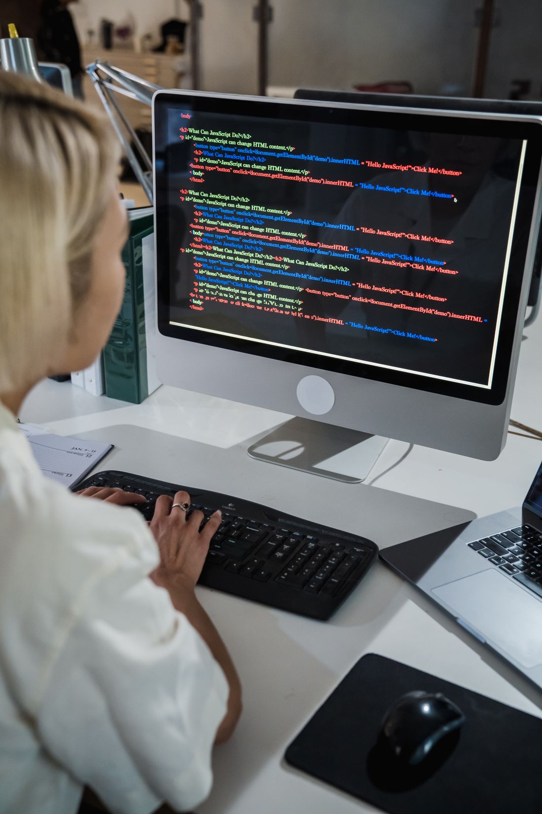A woman types at a desktop computer showing multicoloured code in a bright office