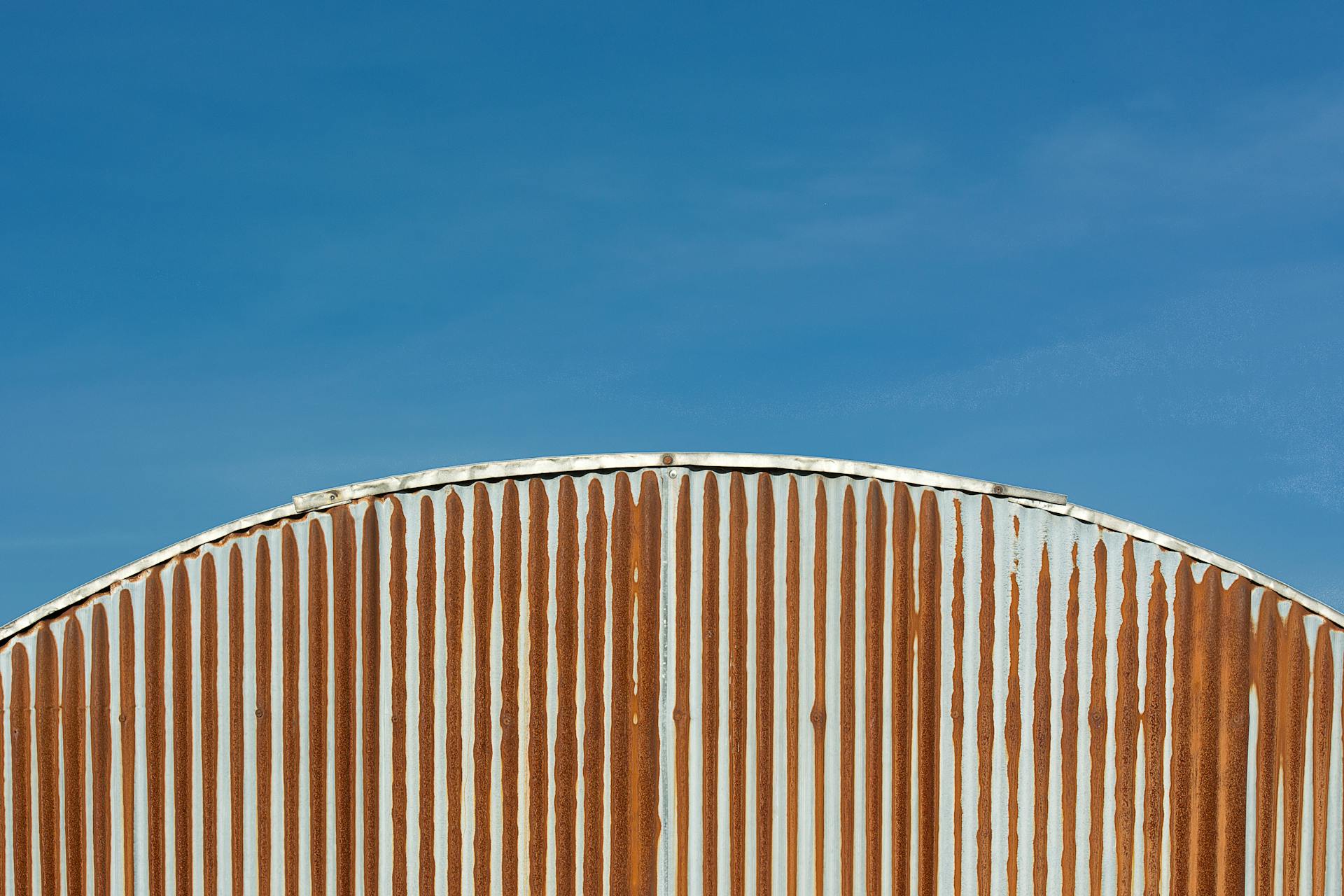 Close-up view of a rusty corrugated metal roof with a clear blue sky background.