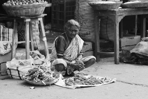 Free An elderly woman vendor sits in a busy Mumbai market surrounded by vegetables. Stock Photo