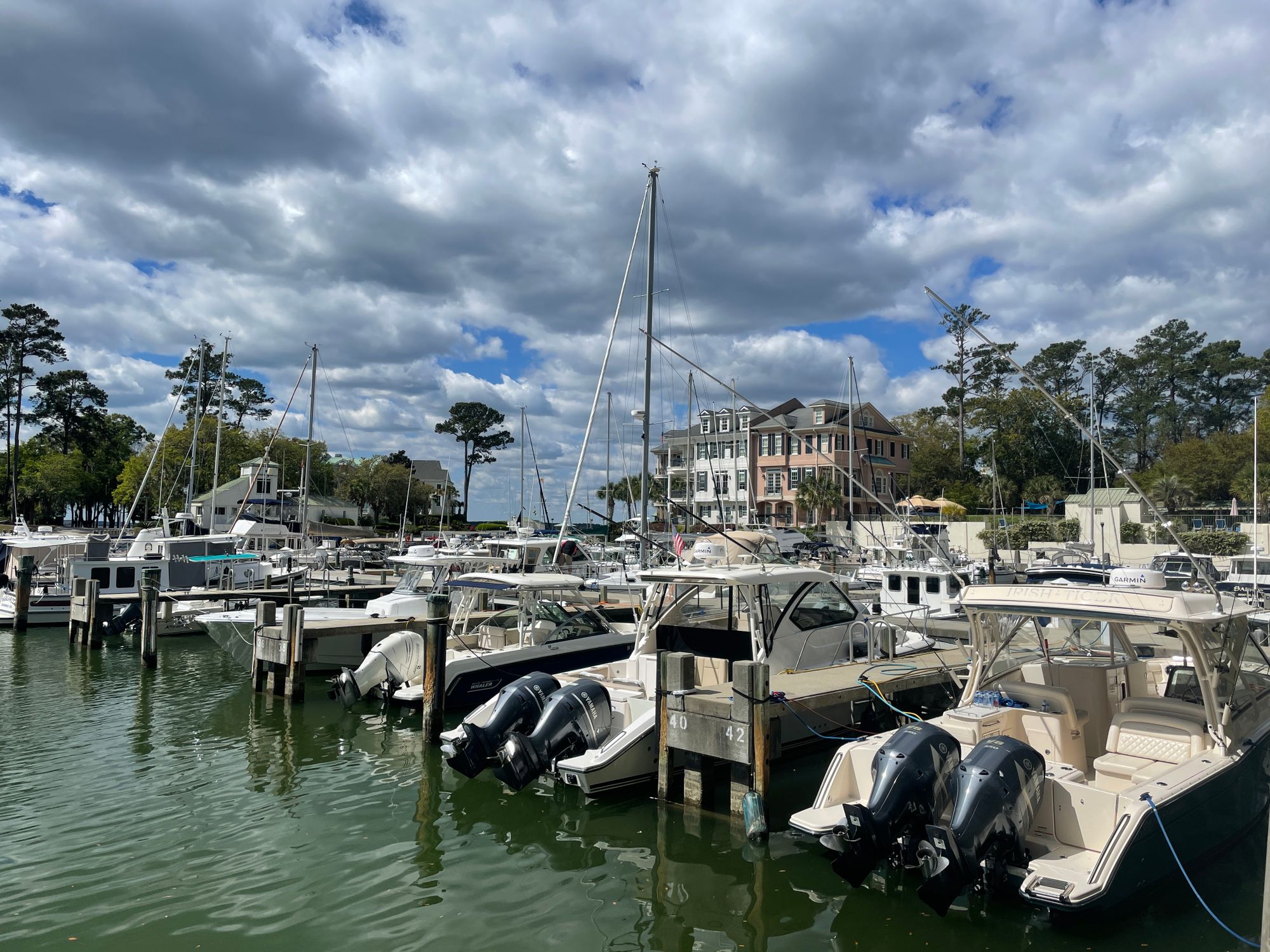 Explore the tranquil marina at Hilton Head Island with docked sailboats and motorboats under a partly cloudy sky