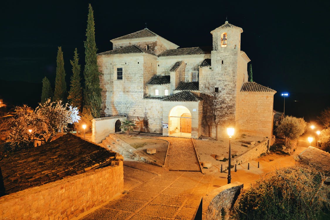 Free Night view of a historic church in Alquézar, Spain, beautifully illuminated and surrounded by trees. Stock Photo