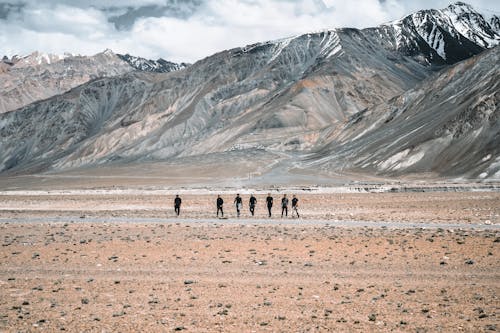 A Group of People Walking on Brown Field Near Gray Mountain