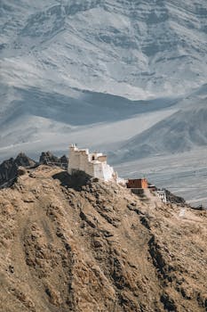 A secluded monastery perched atop a rugged mountain cliff, surrounded by desolate, majestic mountains.