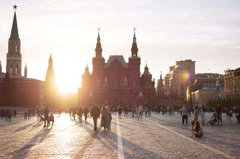 People walking in Red Square, Moscow, with sun setting behind historic buildings, creating dramatic silhouettes.