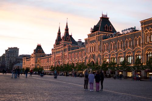 Free View of GUM Department Store lit up at twilight in Moscow's Red Square, with people strolling in the foreground. Stock Photo