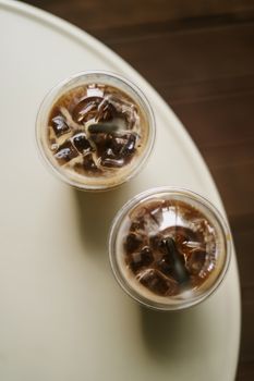 Two refreshing iced coffee drinks with ice cubes viewed from above on a light table.
